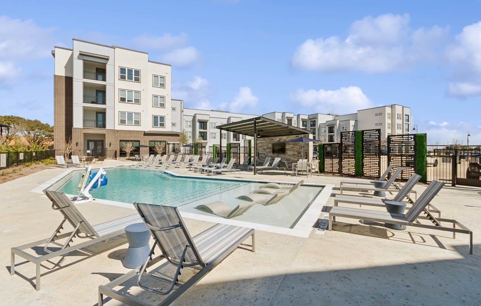 Outdoor community pool at apartment complex with lounge chairs and shade canopy.