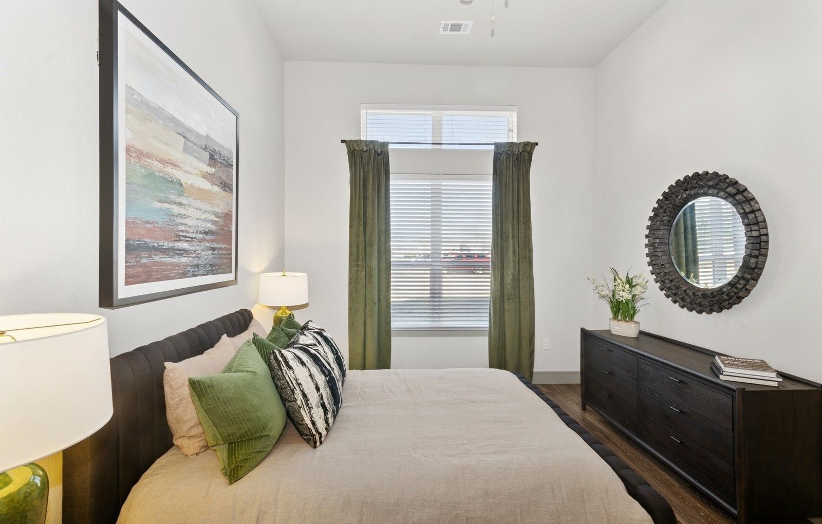 Bedroom in a modern apartment with a bed, dresser, and round mirror.