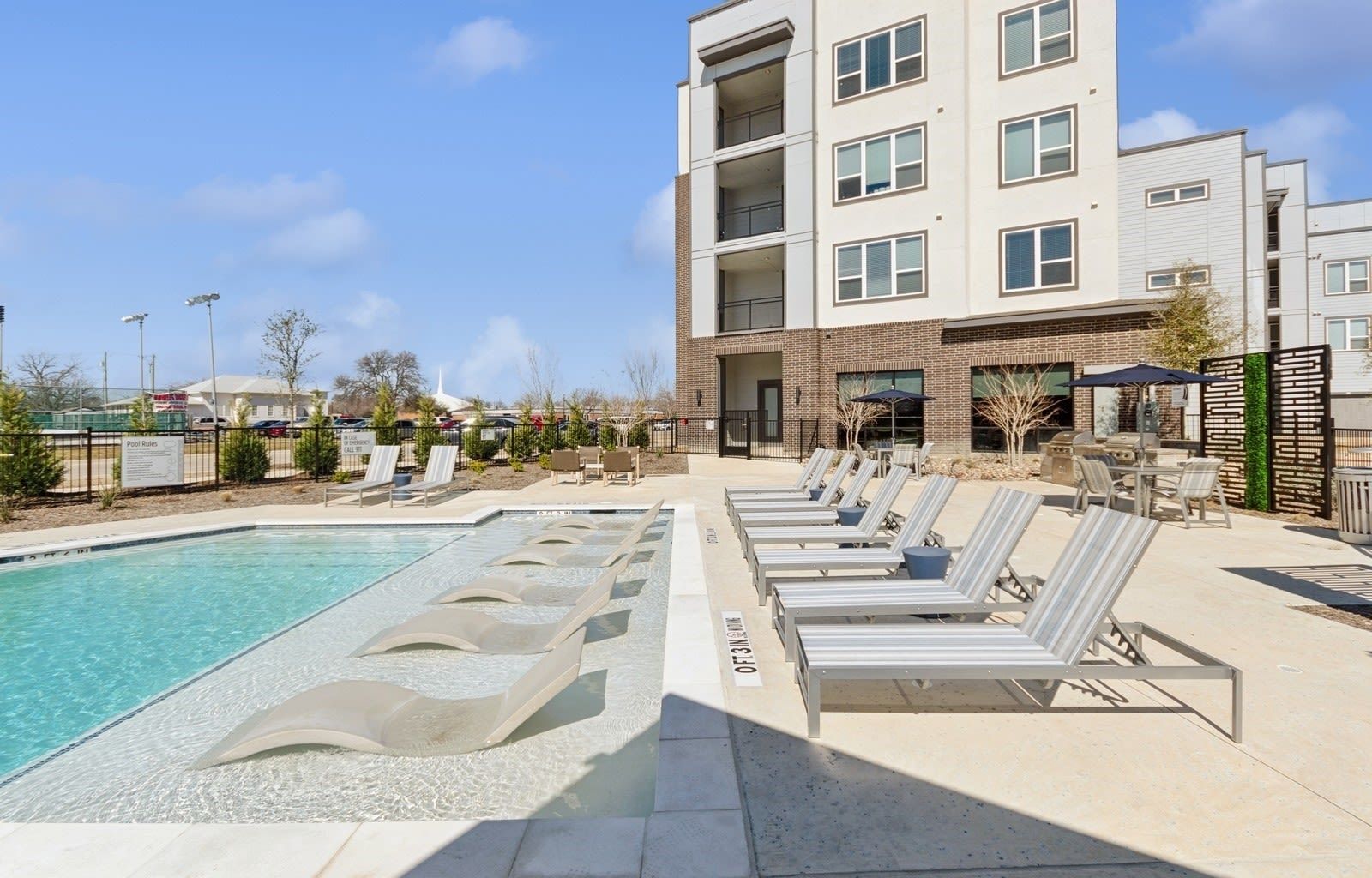 Outdoor apartment pool with lounge chairs and a modern building in the background.