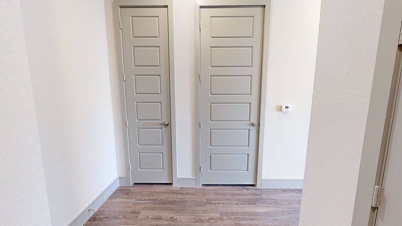 Interior hallway with two paneled gray doors, light walls, and wood-like flooring.