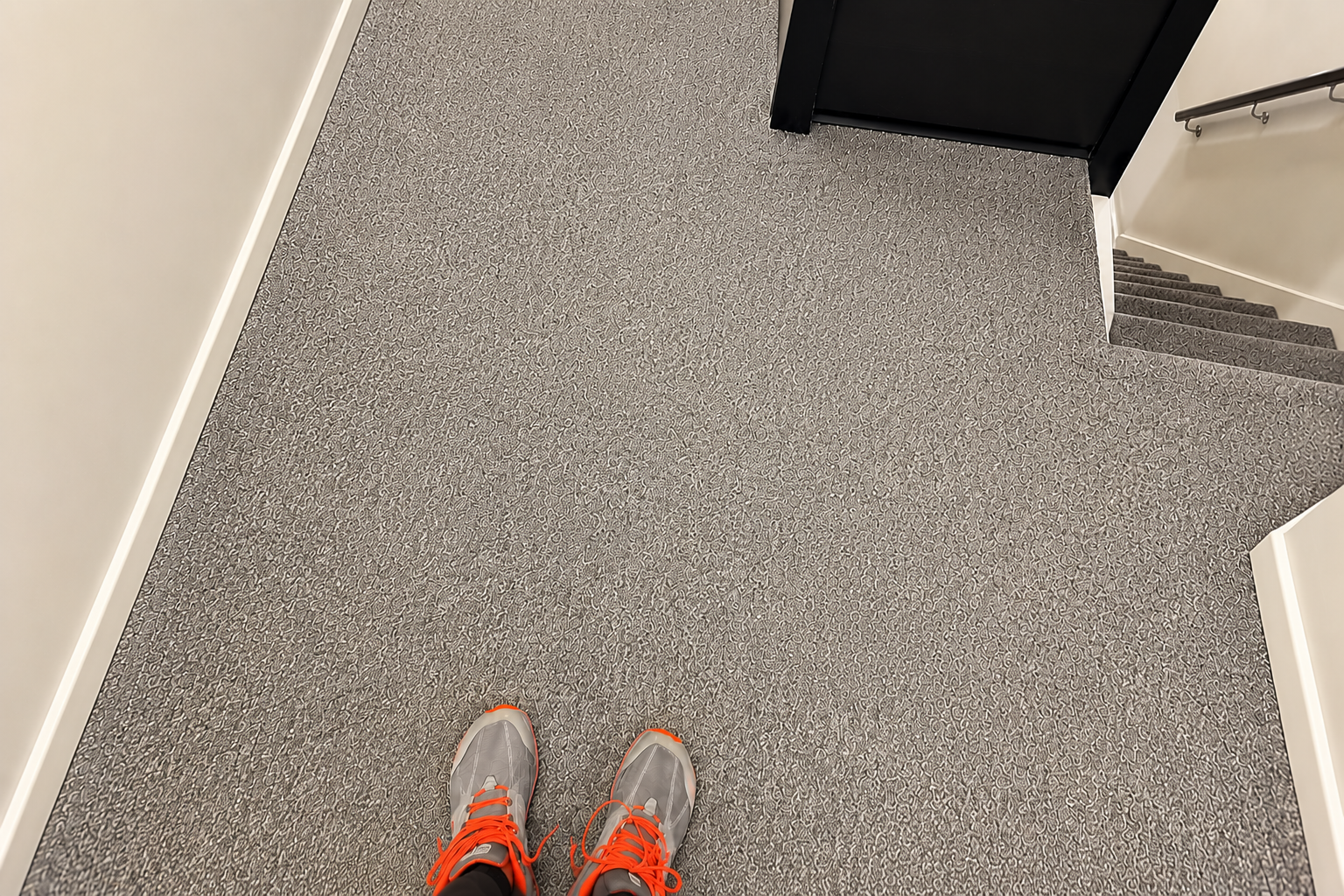 Looking down at gray carpeted hallway with orange sneakers at the bottom edge