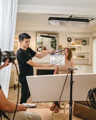 A man is holding a clapper board in front of a woman in a living room.