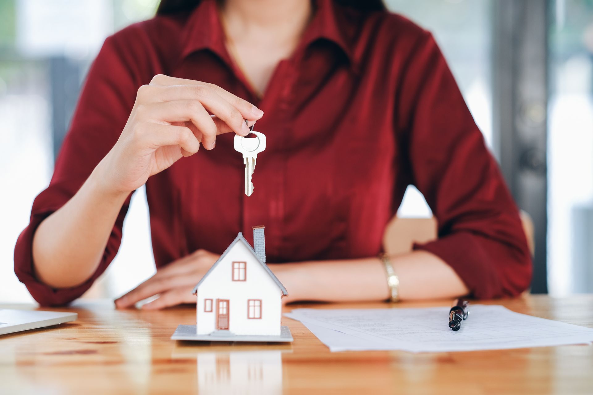 A woman is holding a key in front of a model house.