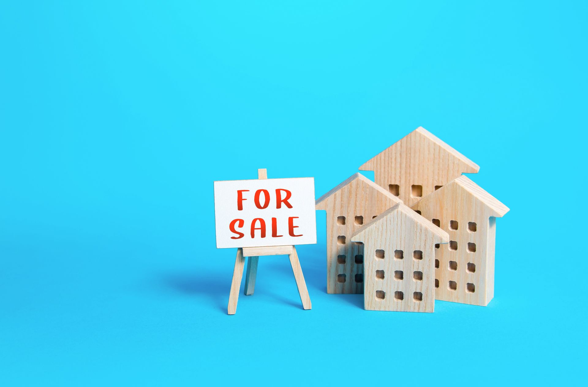 Three wooden houses and a for sale sign on a blue background.