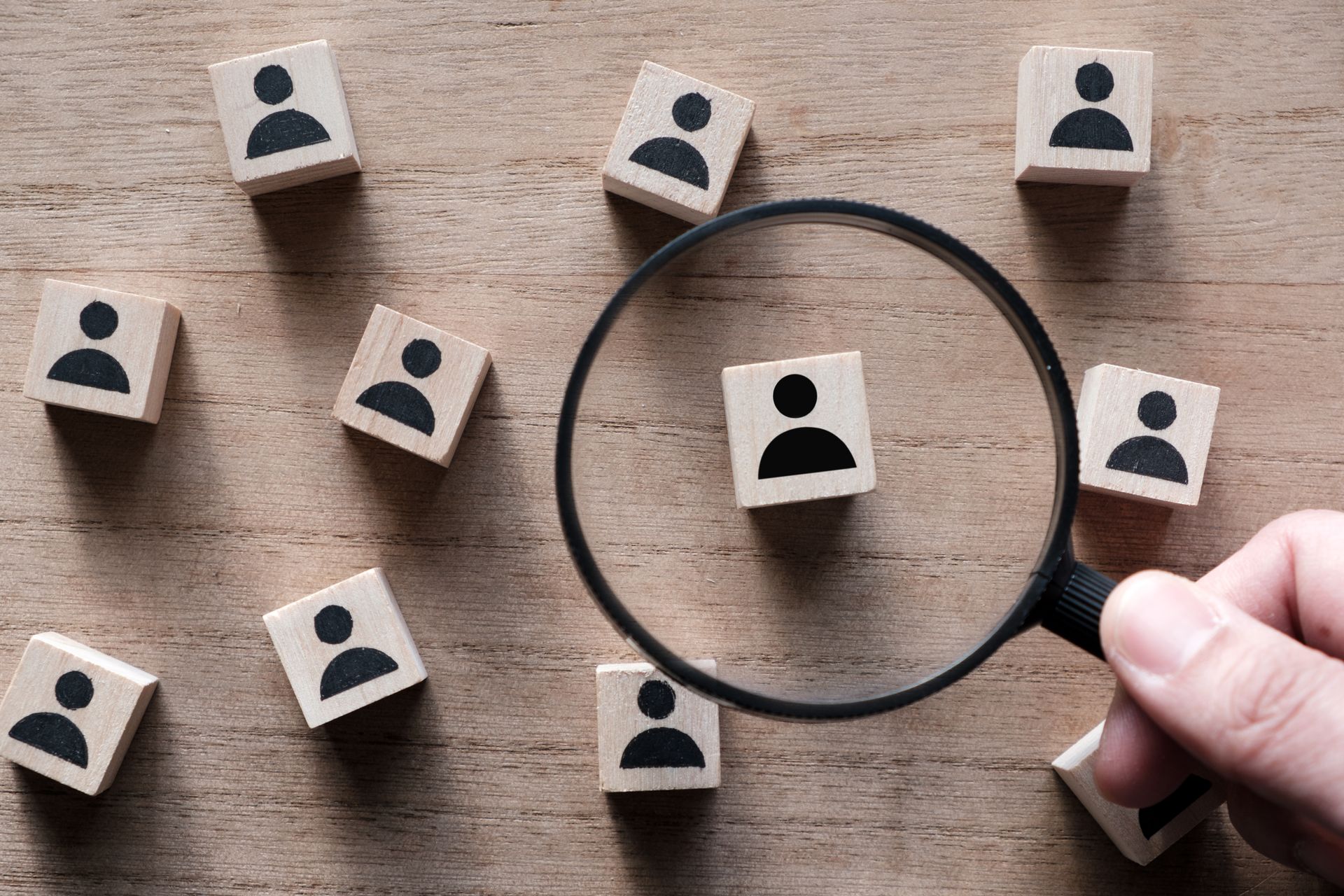 A person is holding a magnifying glass over a group of wooden blocks with people on them.