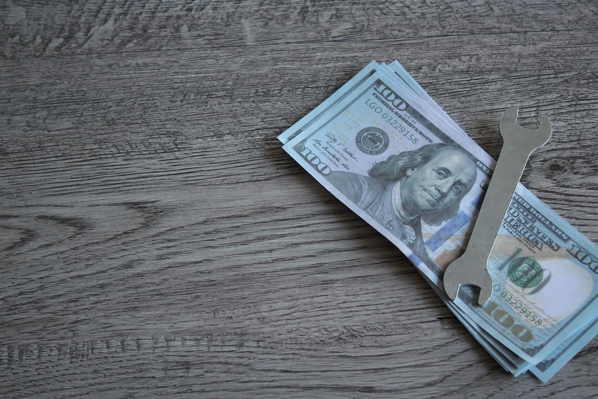 A stack of money and a wrench on a wooden table.