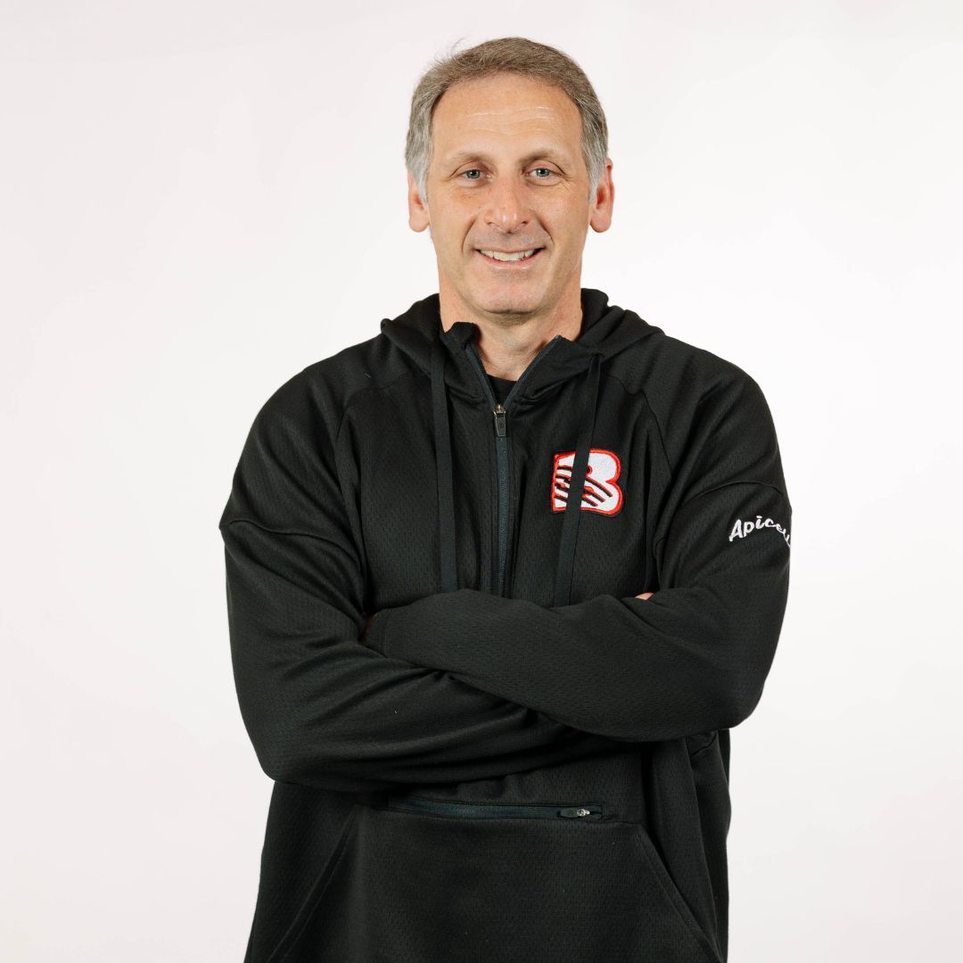 A person with short hair smiling with arms crossed, wearing a black quarter-zip athletic hoodie against a white background.