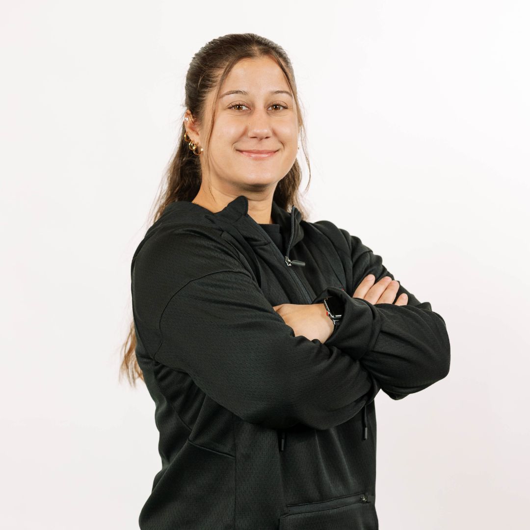 A person smiling with arms crossed, wearing a black hooded sweatshirt against a plain white background.