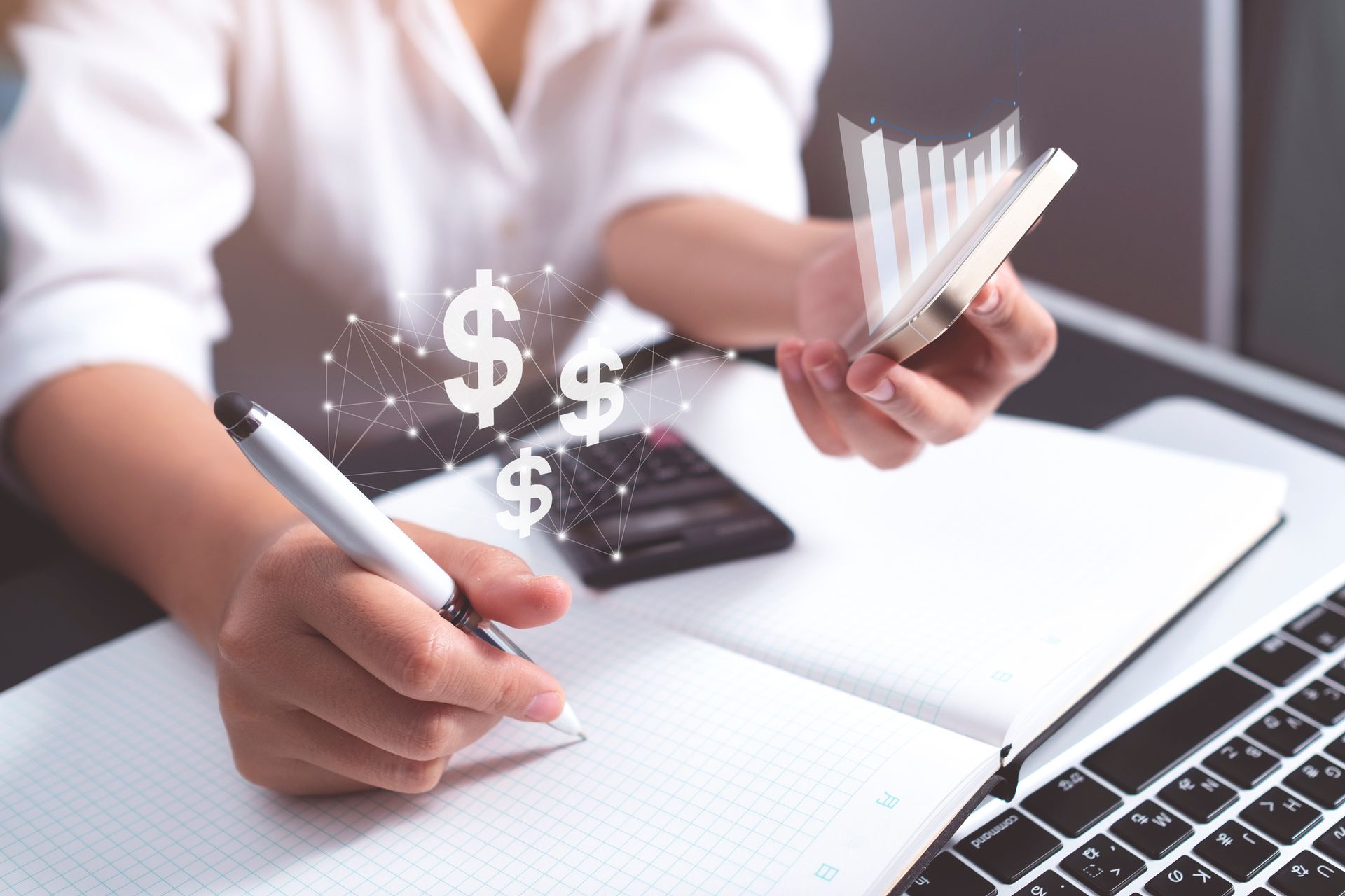 Person writing in a notebook, dollar signs floating above, small calculator and laptop visible.