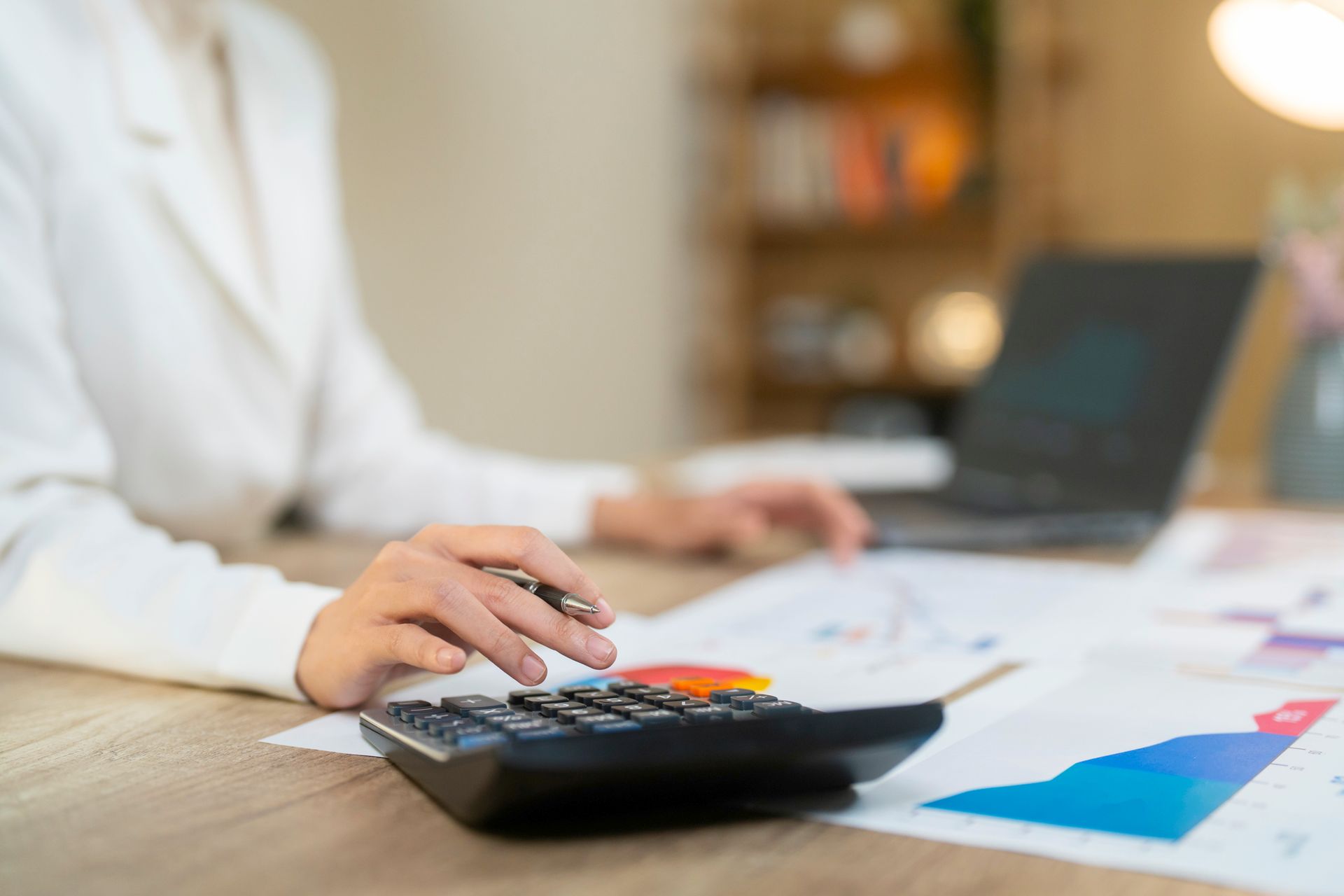 Tax planning professional using calculator and reviewing financial charts beside laptop on desk.