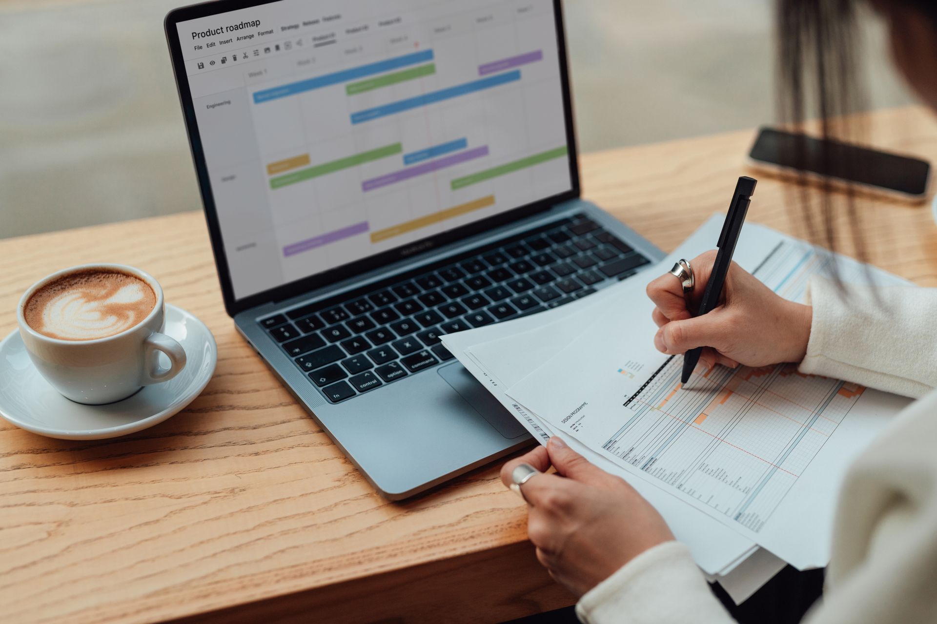 Tax planning professional reviewing financial papers beside laptop displaying project timeline. Tax planning professional reviewing financial papers beside laptop displaying project timeline.