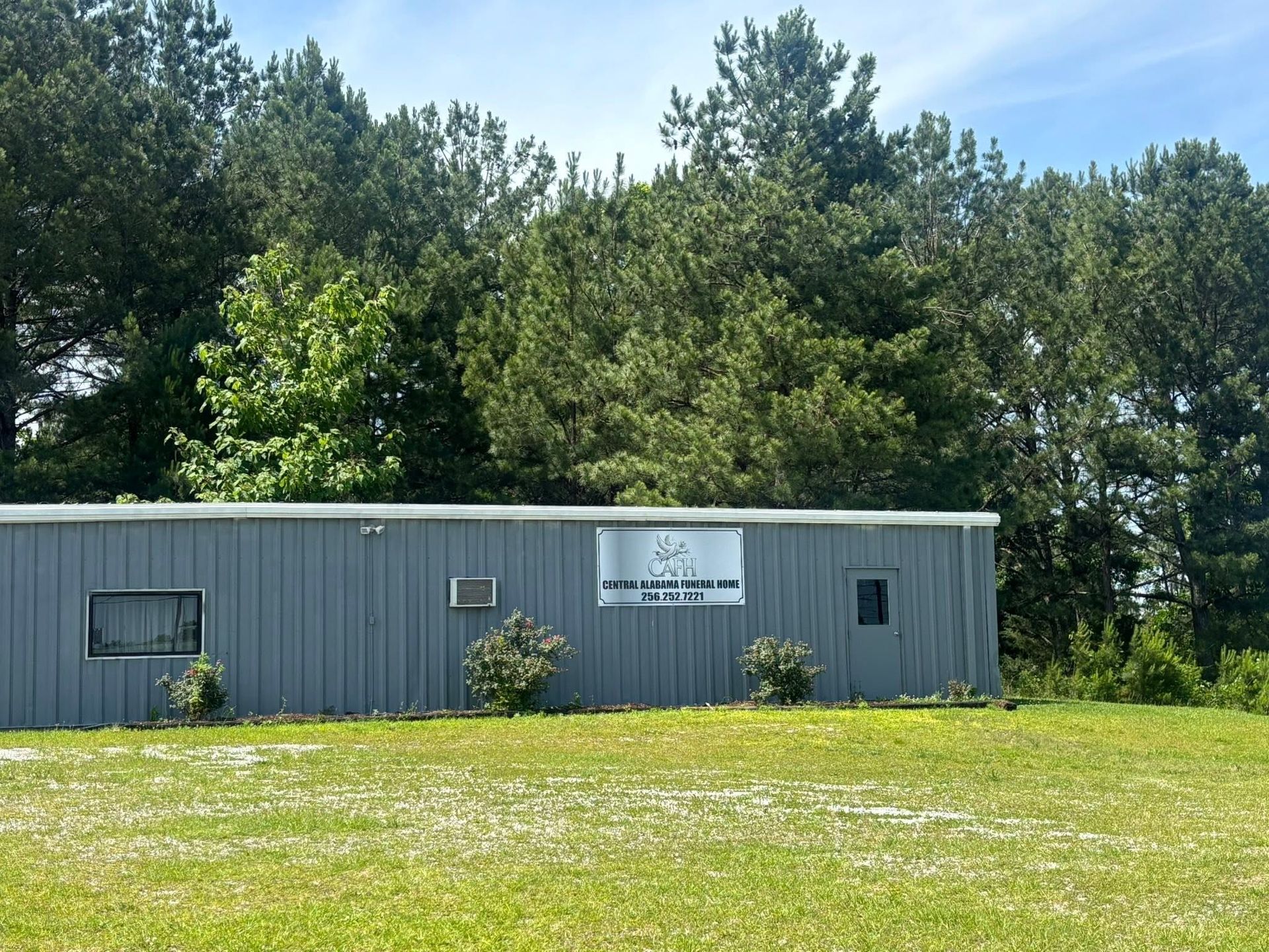 Gray metal building in a grassy field with trees behind it and a sign on the front.