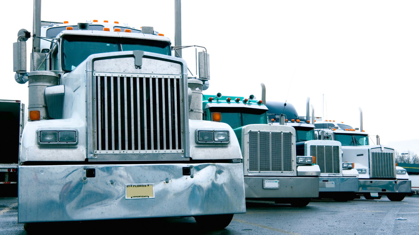 Semi-trucks parked in a row on a cloudy day.
