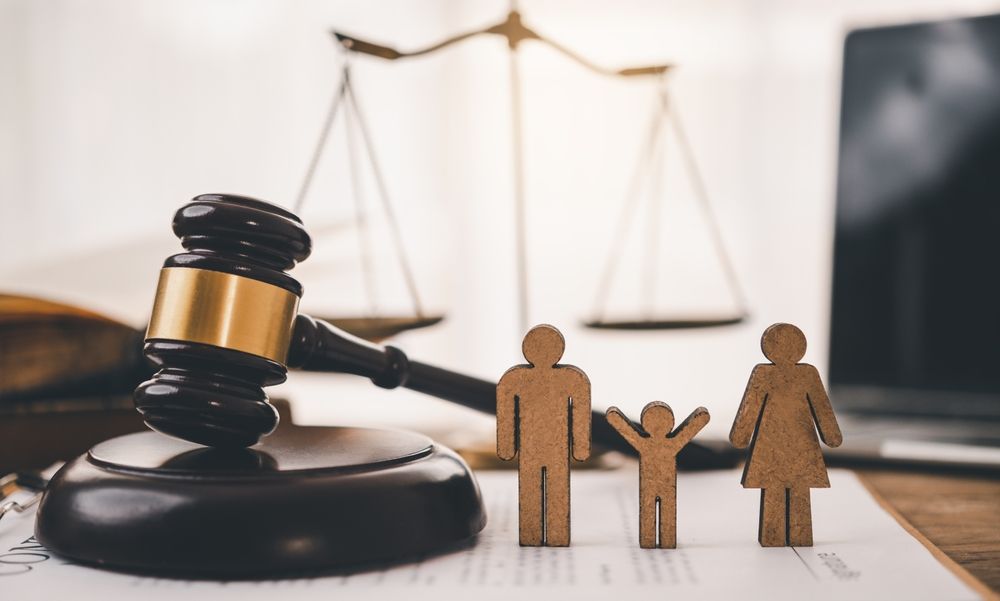 A wooden family is sitting next to a judge 's gavel and scales of justice.