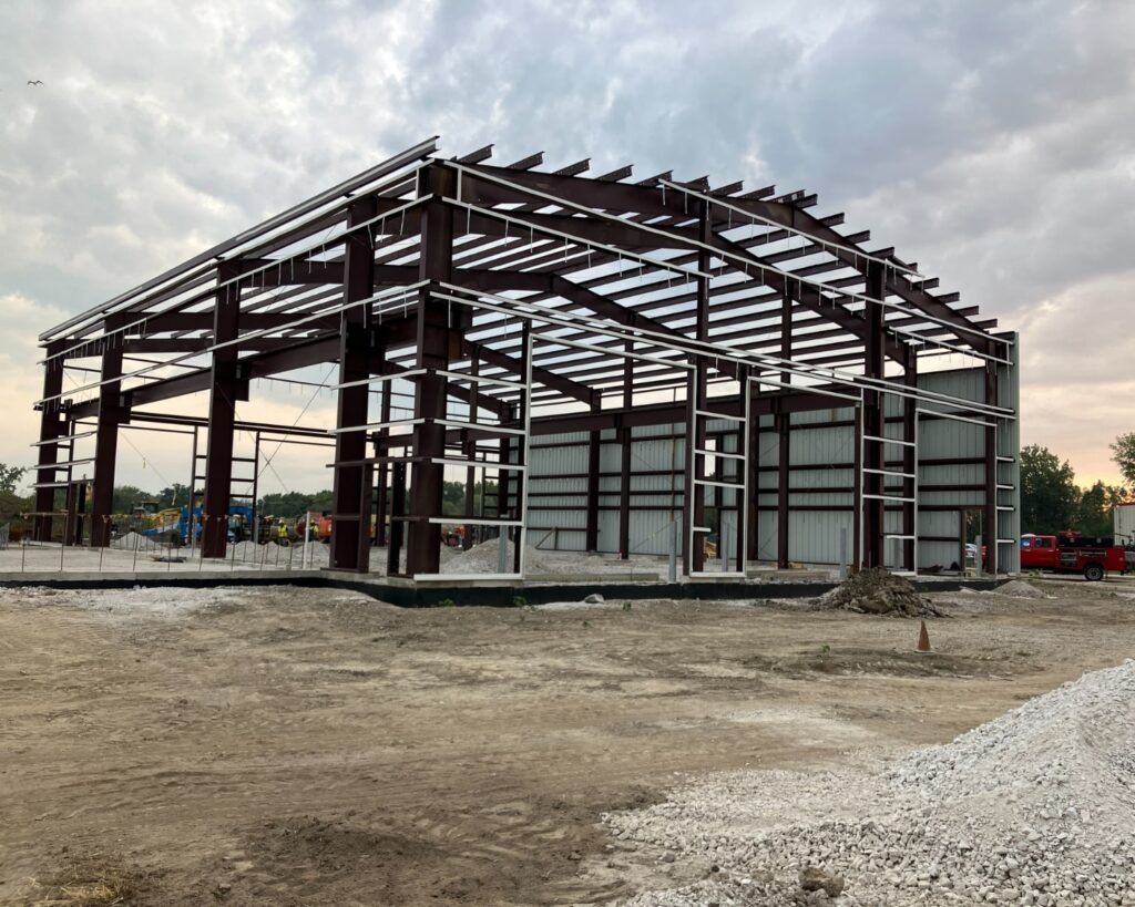 Steel frame of a large building under construction against a cloudy sky.