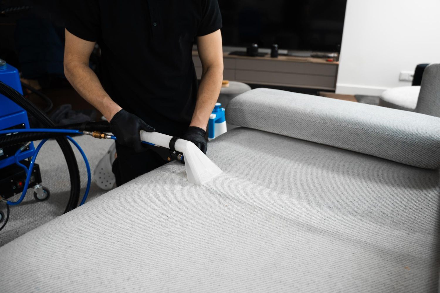A man is cleaning a couch with a vacuum cleaner.