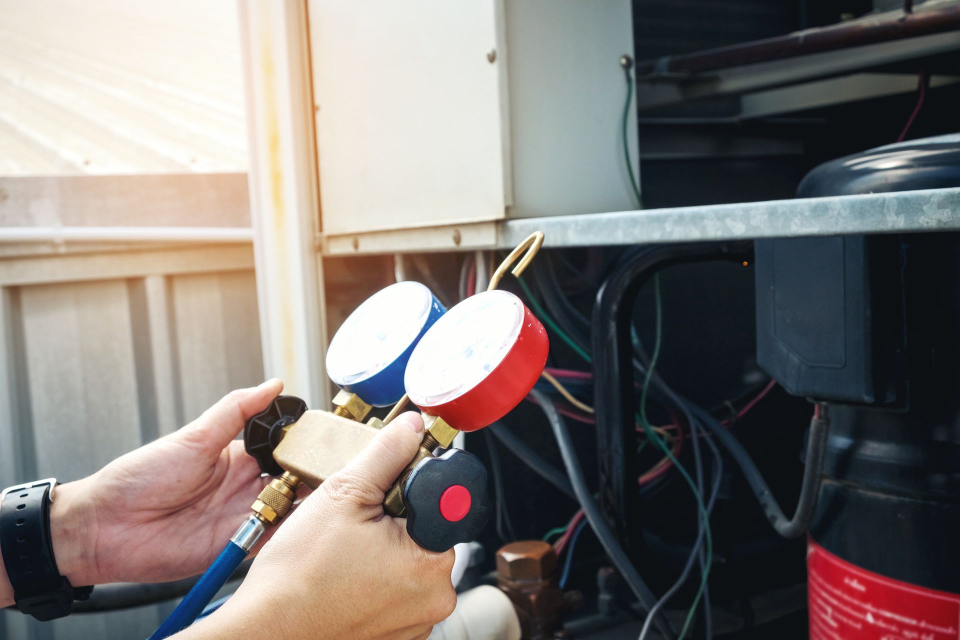 Hands using gauges to check air conditioning unit.