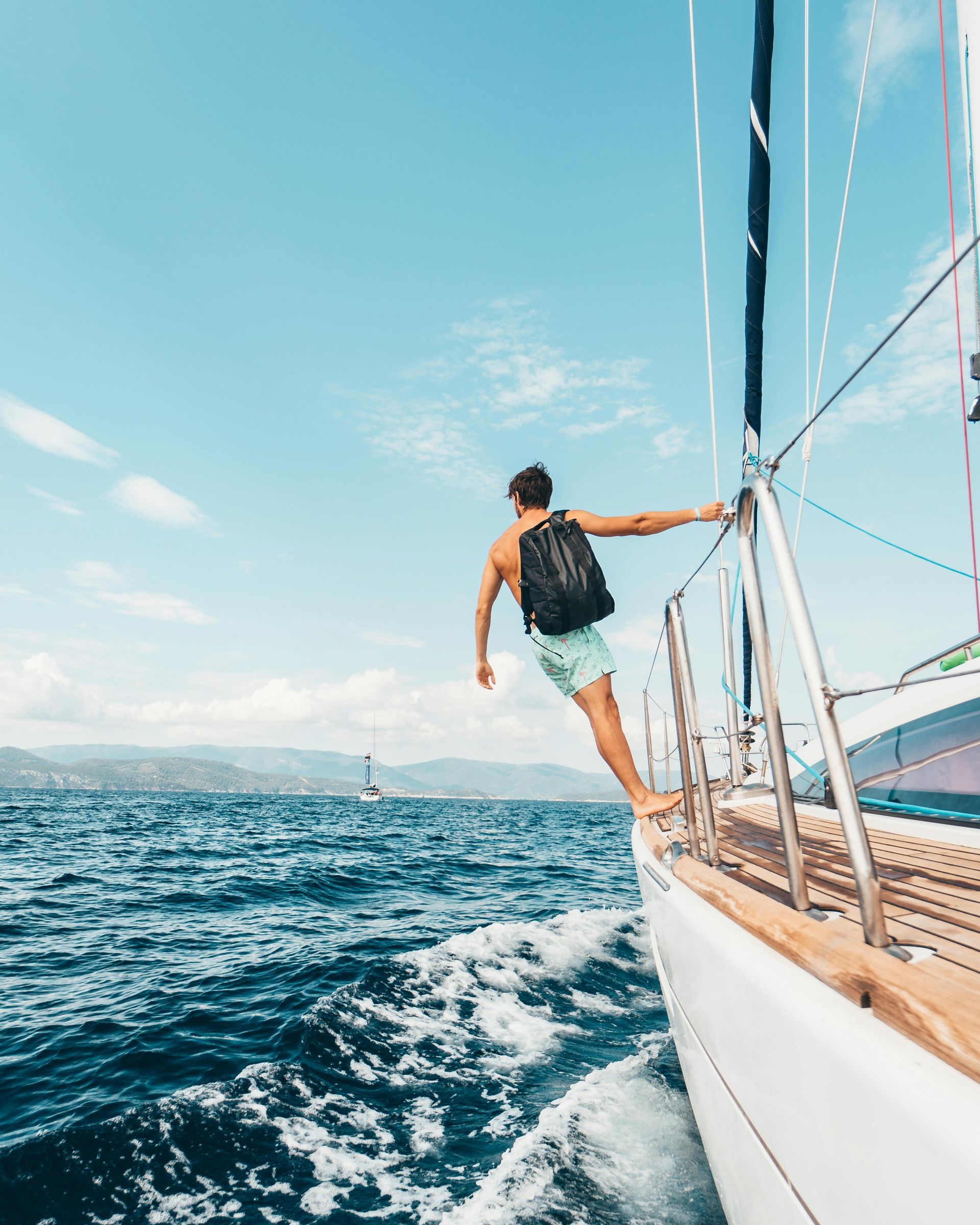 A man is standing on the side of a sailboat in the ocean.