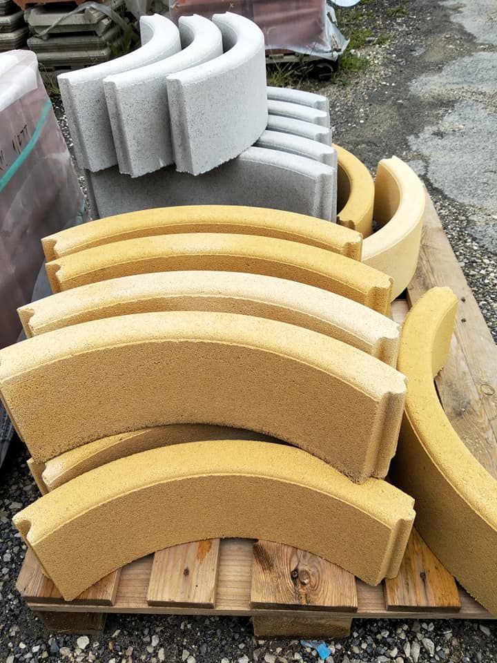Blocchi di cemento curvi gialli e grigi impilati su un pallet di legno, probabilmente per uso edile.