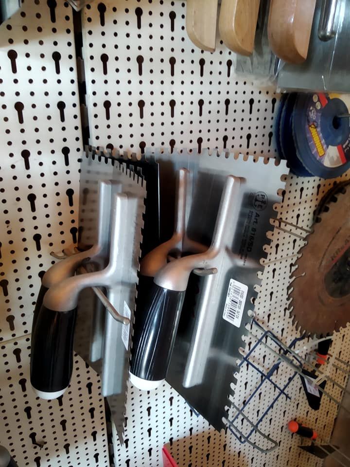 Due cazzuole dentate appese a un pannello forato, insieme ad altri utensili.