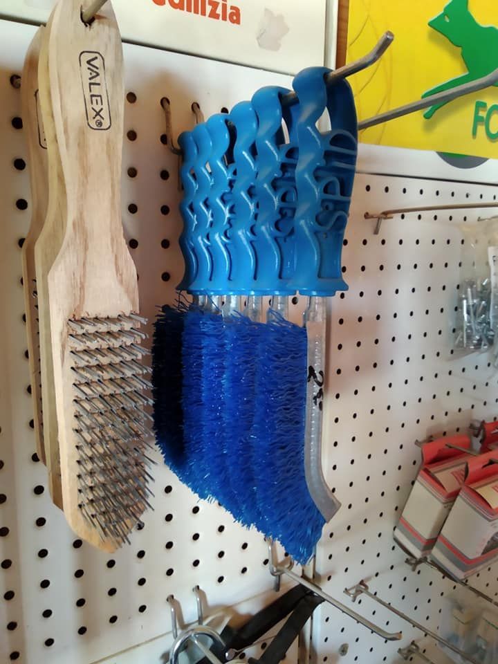 Spazzole con manico in legno e spazzola blu appese a un pannello forato in un negozio.