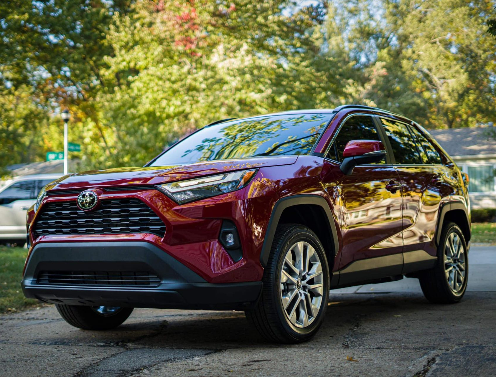 Red Toyota RAV4 parked on a street, trees in the background.