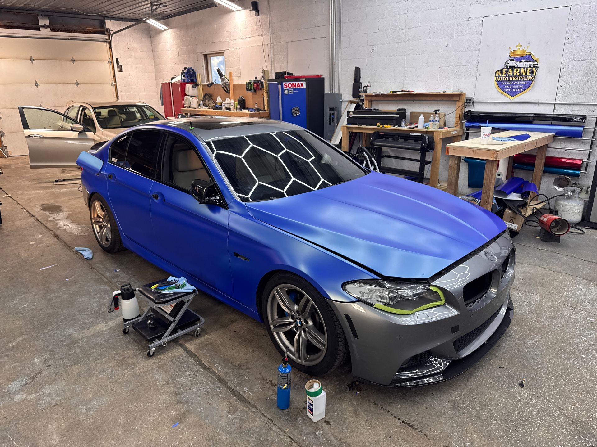 Blue vinyl color-change wrap being installed on a BMW sedan inside Kearney Auto Restyling in Kearney