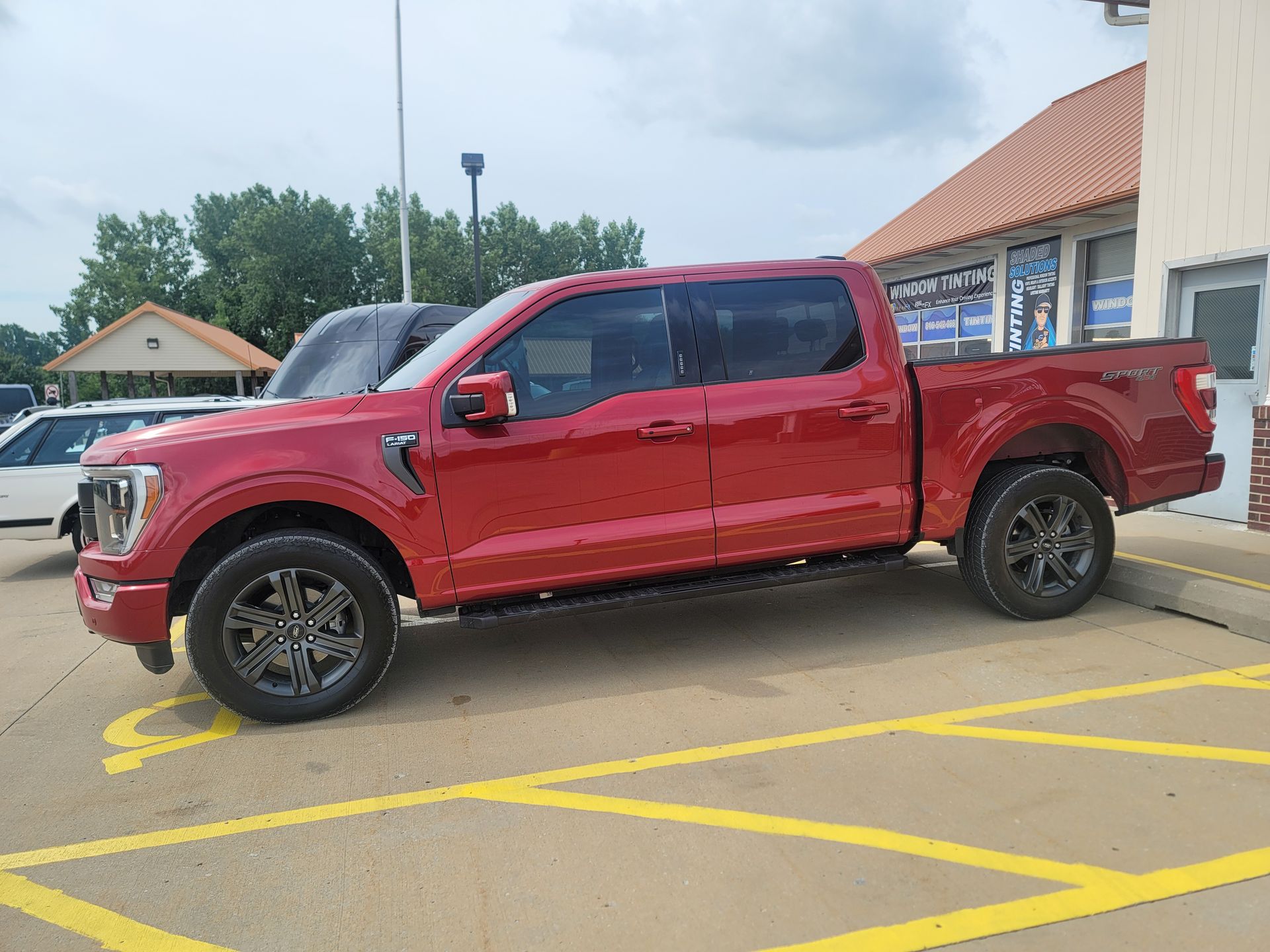 Red Ford F-150 pickup truck parked in a yellow-lined parking space. Dark-tinted windows, black wheels, and a building in the background.