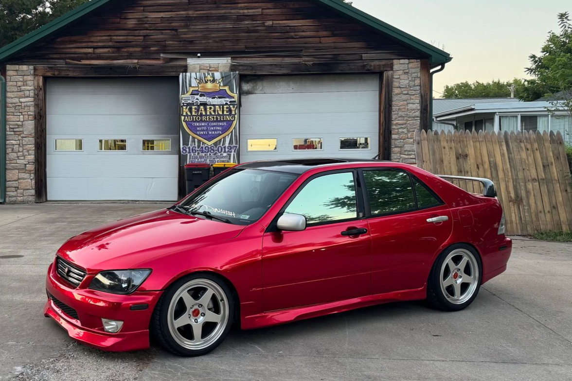A red sports car parked in front of an old garage with white doors.