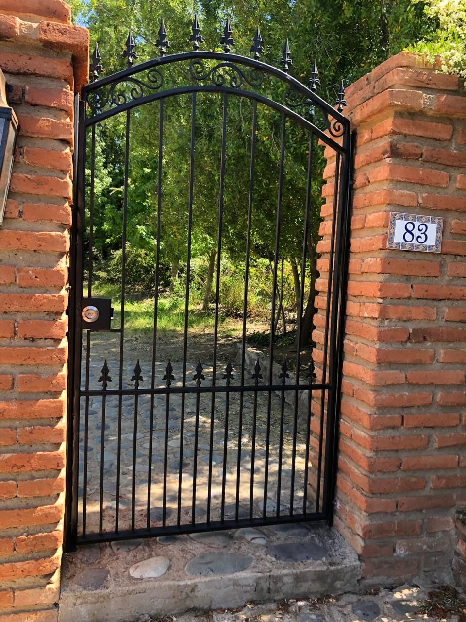 Una verja de hierro negro entre pilares de ladrillo, con el número 93, da acceso a un sendero arbolado.