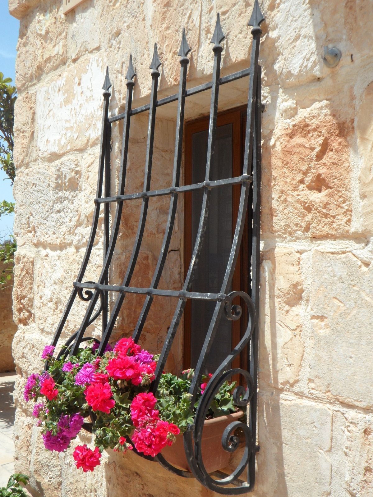 Reja de hierro forjado negro con flores rosas sobre una pared de piedra.