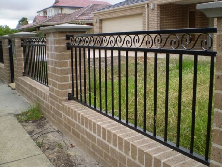 Valla frontal de ladrillo con barandillas de metal negro a lo largo de una acera y un patio con césped.