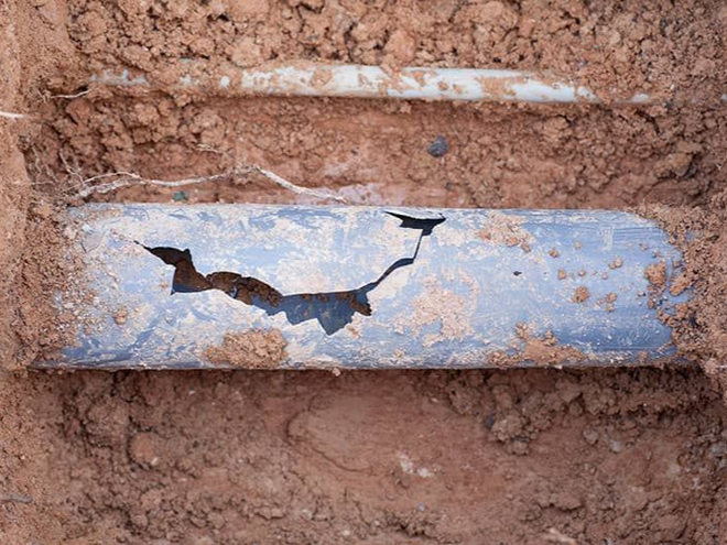 A broken blue pipe in a trench filled with brown soil.
