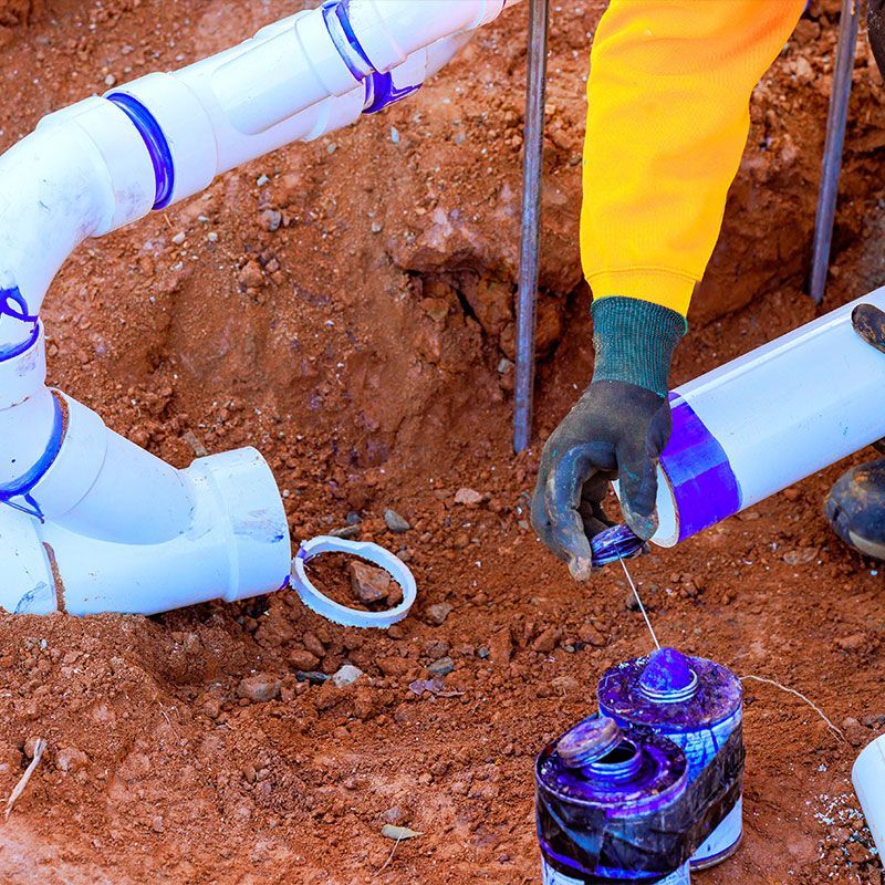 Worker connects new plumbing sewage pipes while fixing drainage system in residential yard during work day