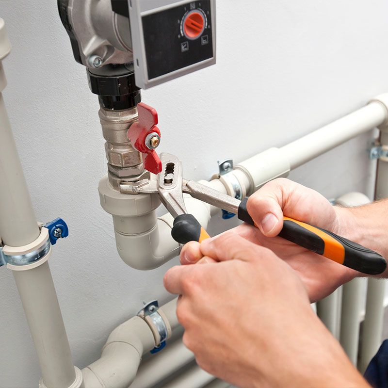 The man is installing the heater system in the house and checking pipes by the wrench