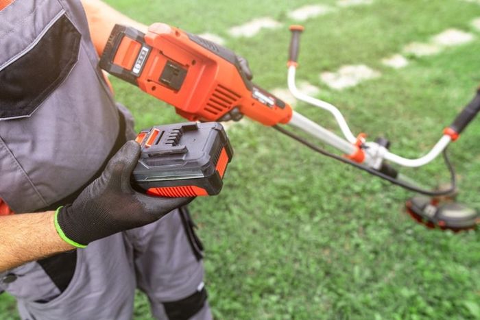 A man is holding a lawn mower with a battery attached to it.