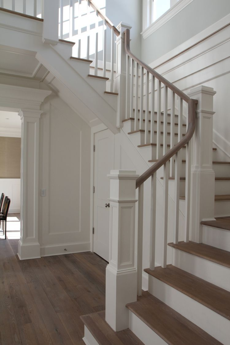 White staircase with wooden steps, white railings, and dark hardwood floor in a bright interior hallway