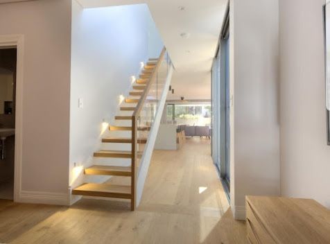 Modern hallway with wooden staircase, light wood floors, and bright open interior leading to a dining area