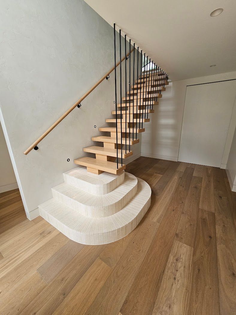 Modern indoor staircase with wooden treads, metal balusters, and a curved white base in a bright room
