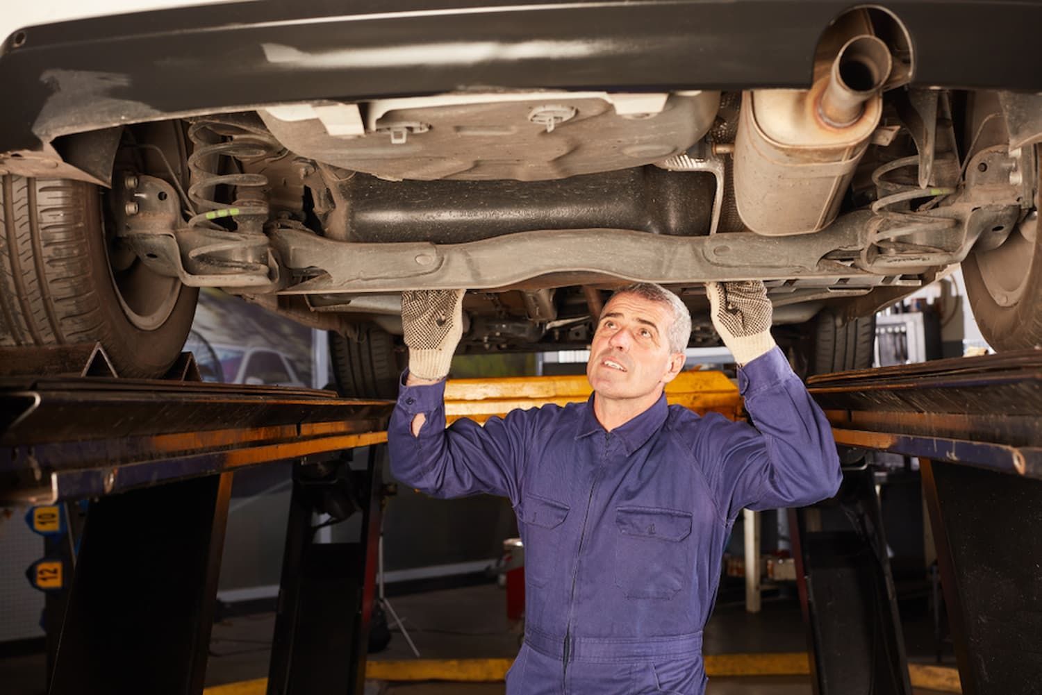 A Man Is Working Under a Car on A Lift in A Garage — Chinderah Smash Repairs in Chinderah, NSW