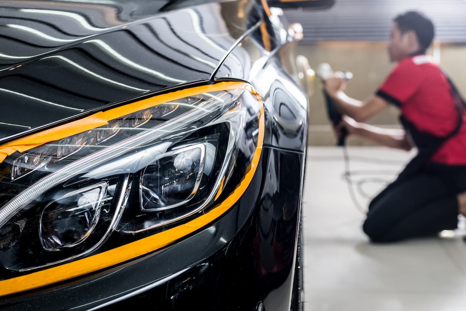 A Man Is Polishing a Black Car in A Garage — Chinderah Smash Repairs in Chinderah, NSW