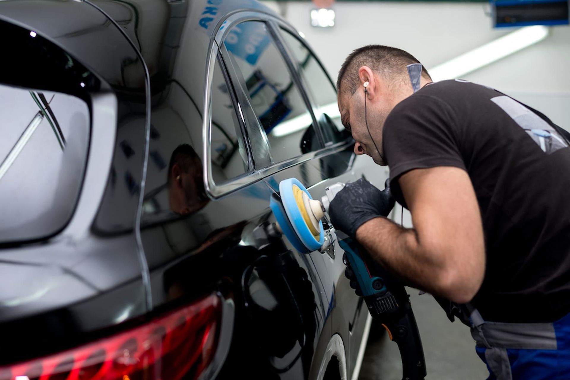 A Man Is Polishing a Black Car with A Machine — Chinderah Smash Repairs in Chinderah, NSW