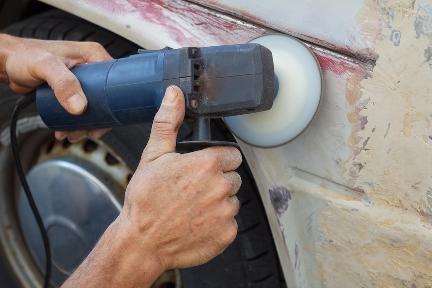 A Man Is Holding a Piece of Wood Over the Hood of A Car — Chinderah Smash Repairs in Chinderah, NSW