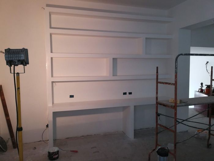 Parete bianca parzialmente rifinita con mensole a muro in una stanza in costruzione