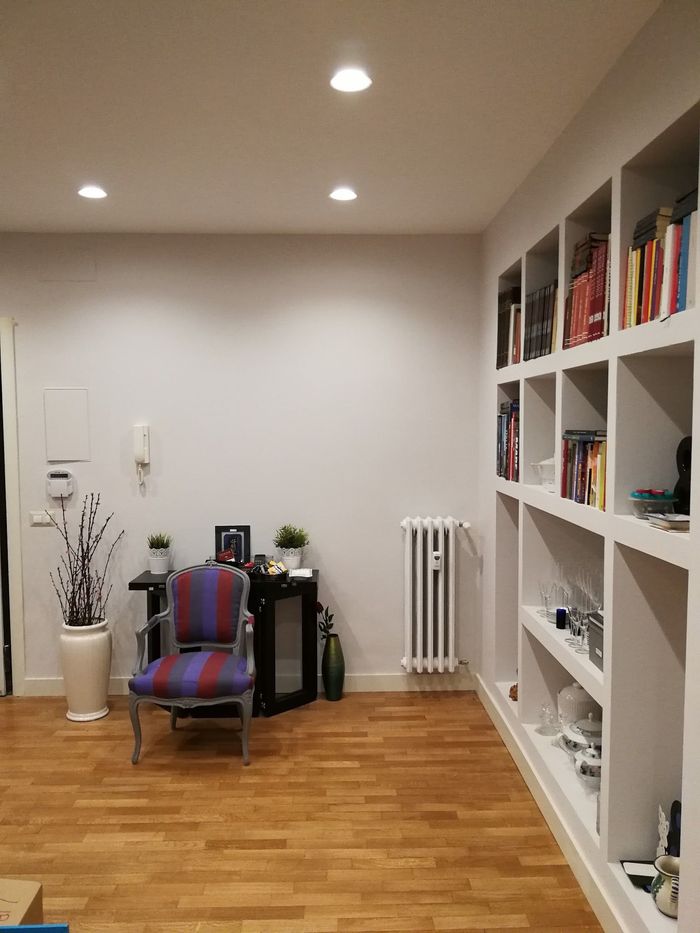 Luminoso soggiorno con librerie, una poltrona a righe, una lampada da terra e pareti bianche su pavimento in legno.