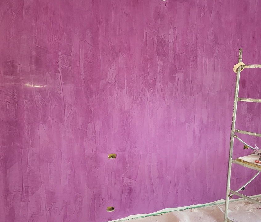 Parete dipinta di viola in una stanza, con un'impalcatura metallica e prese elettriche vicino alla base.