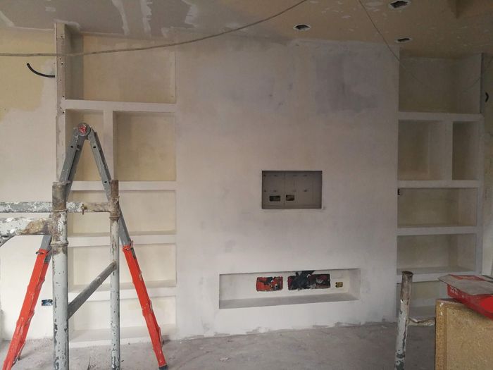 Interno in fase di ristrutturazione con scala, scaffali a muro e nicchia per la TV.