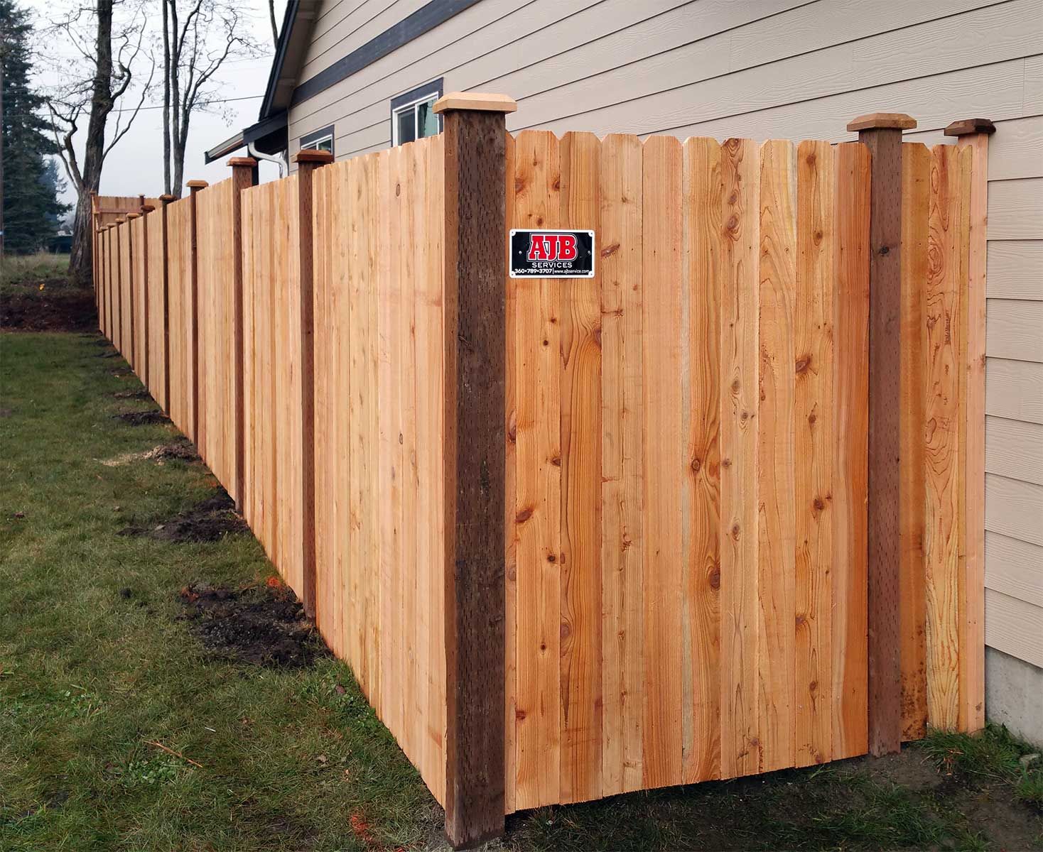 Wooden fence along a house, with green grass in front.