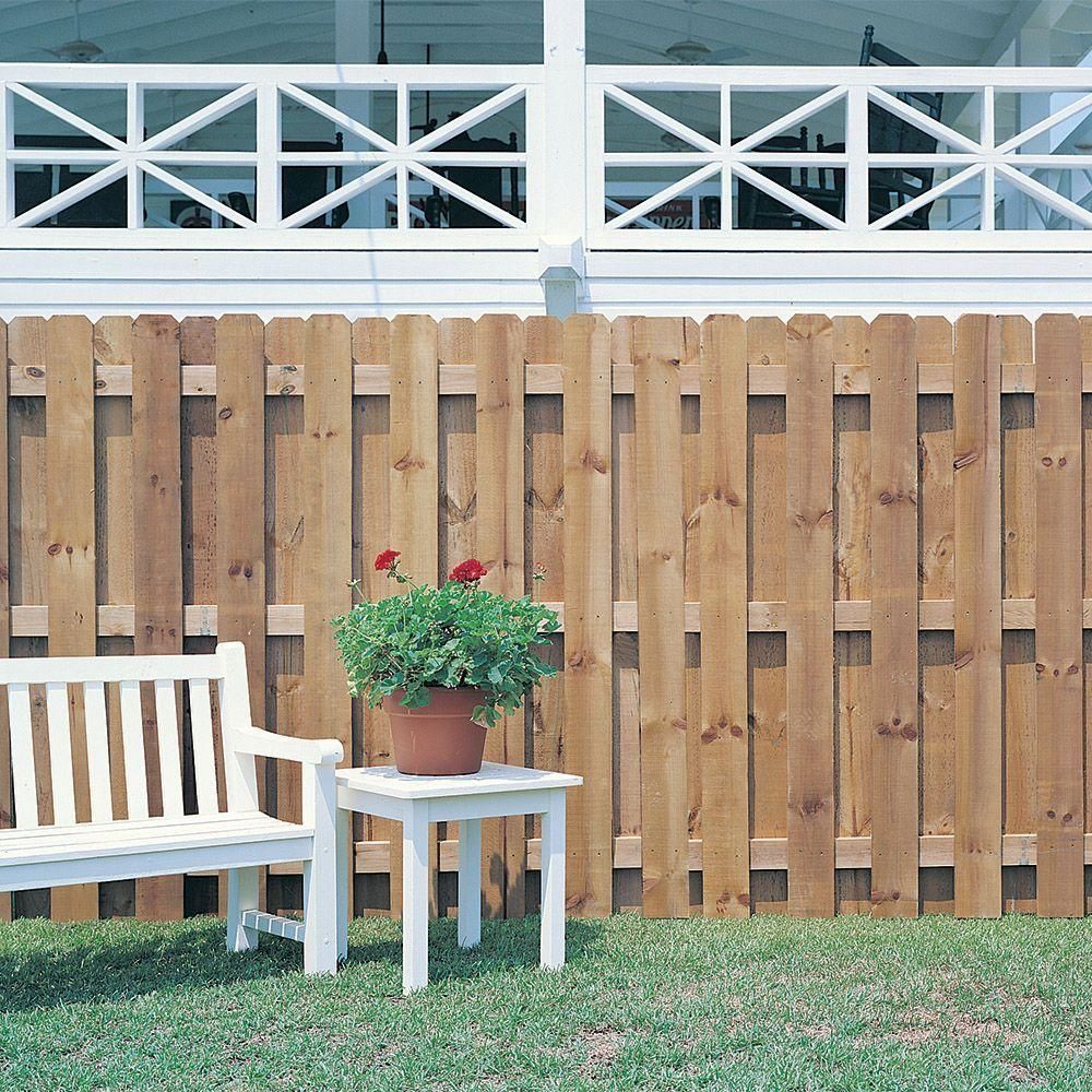 White bench and table with potted flowers in front of a wood fence, beneath a white porch.
