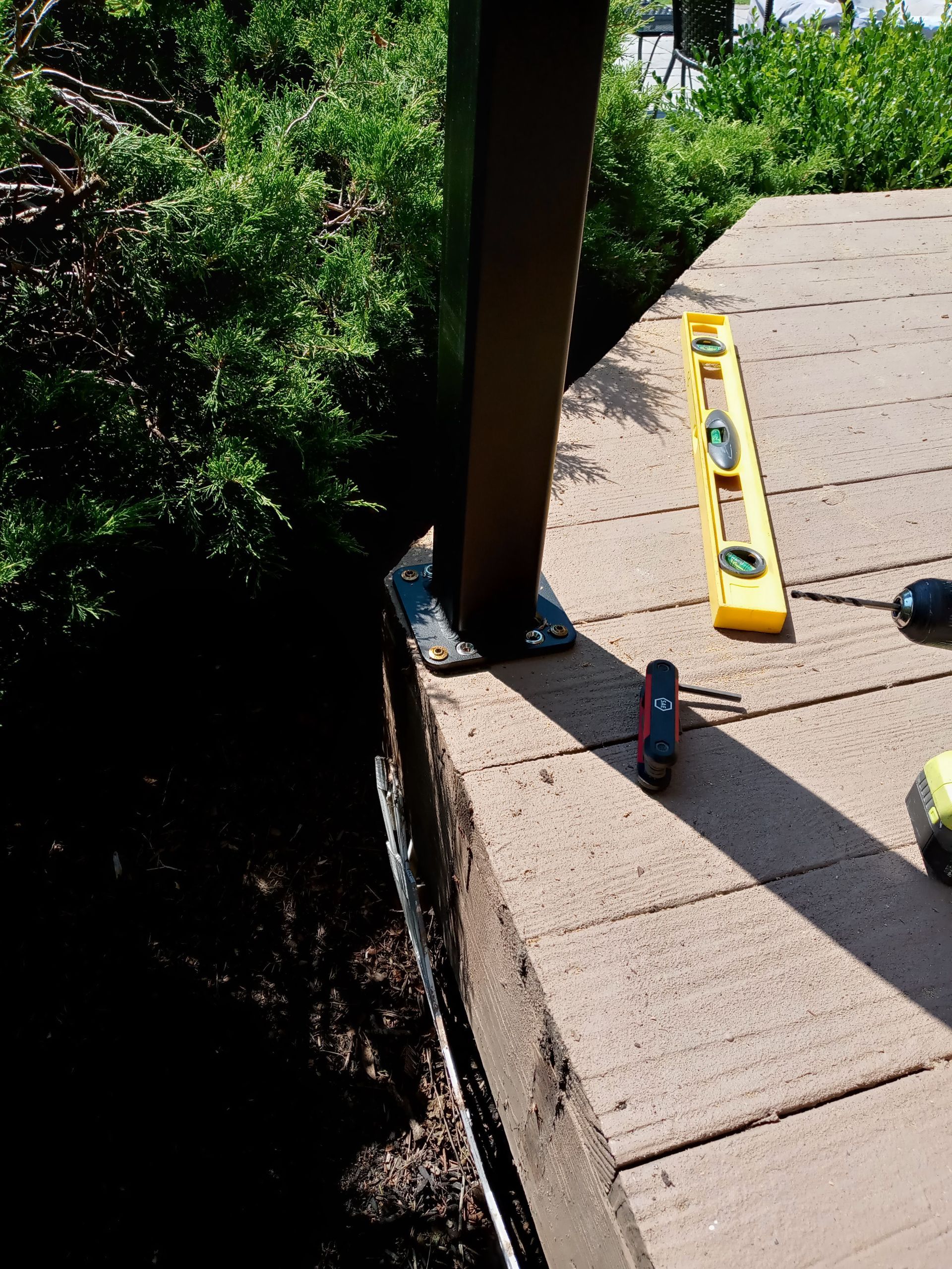 A dark post secured to a paver patio with a level, screwdriver and other tools nearby.
